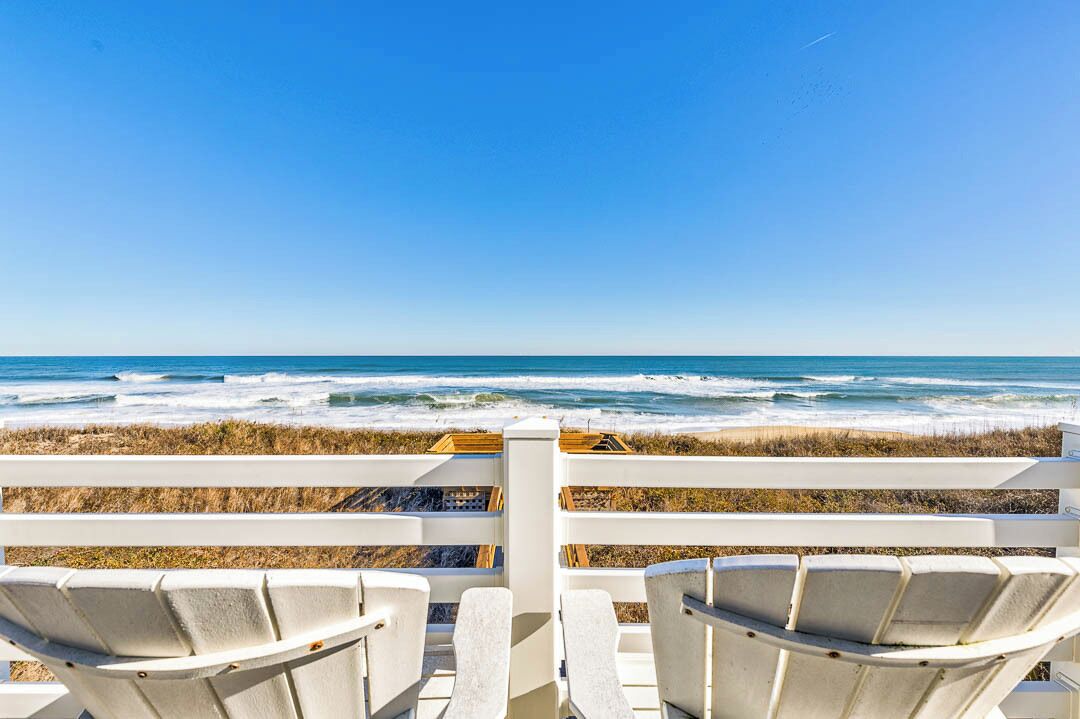 A beach view with white chairs and a wooden fence.