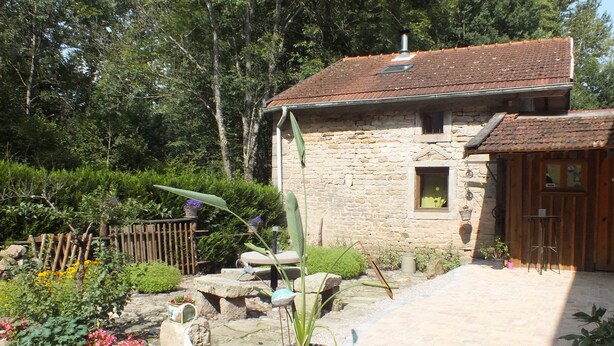 Ein Steinhaus mit einem Ziegeldach, umgeben von einem Garten mit verschiedenen Pflanzen und einem Holzzaun.