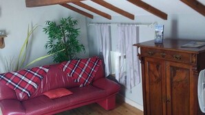 Ein gemütliches Wohnzimmer mit einem roten Sofa, Holzbalken, einem kleinen Holztisch und einem Schrank.