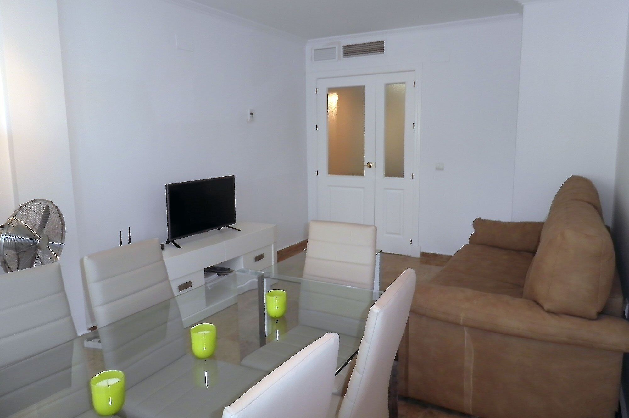 A living room with a flat-screen TV, a glass coffee table with two yellow cups, a brown sofa, and a white cabinet.