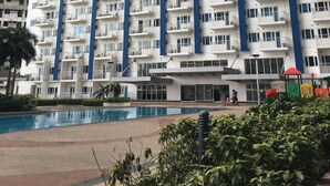 A high-rise residential building with multiple balconies, a swimming pool, and a landscaped area with plants. - Cool Place Light Residences (Mandaluyong)