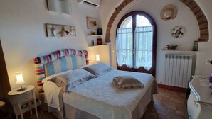 Une chambre avec un plafond en briques, un lit doté d’une tête de lit à rayures, une table de chevet avec une lampe et une fenêtre donnant sur l’extérieur.