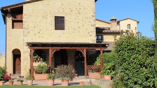 Un bâtiment en pierre doté d’un porche abrité et de plantes en pot.