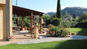 Un espace extérieur aménagé avec des sièges, protégé par un toit, doté d’un sol en pierre, entouré de plantes en pot et d’une pelouse.