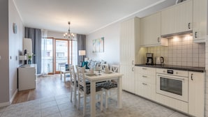 A modern kitchen with white cabinets, a built-in oven, and a dining area with a table set for four.
