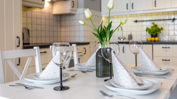 A dining table set with white plates, silverware, and wine glasses, with a vase of white tulips in the center.
