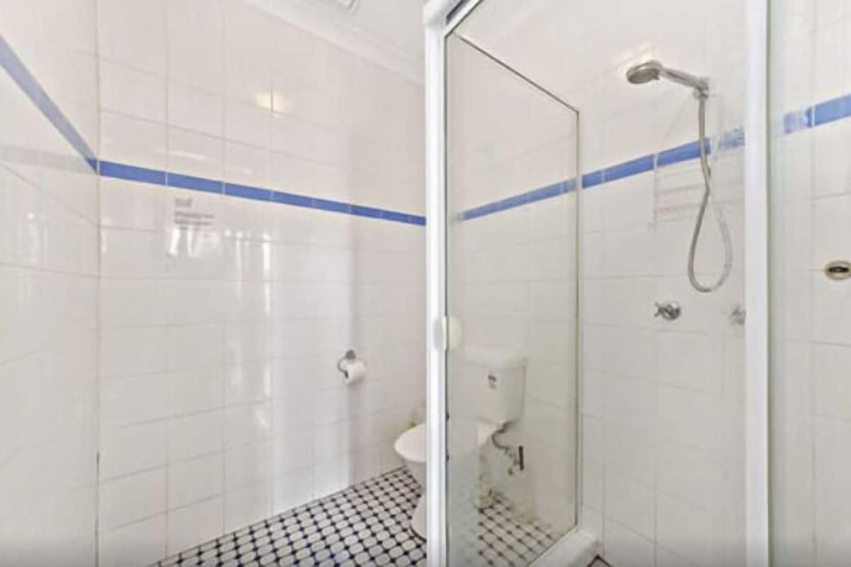 A glass-enclosed shower with a handheld showerhead, a white tiled wall with blue stripes, and a black and white checkered floor.