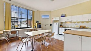 A modern kitchen with a dining area, large windows, and a view of the street. - Sinclairs City Hostel (Surry Hills)