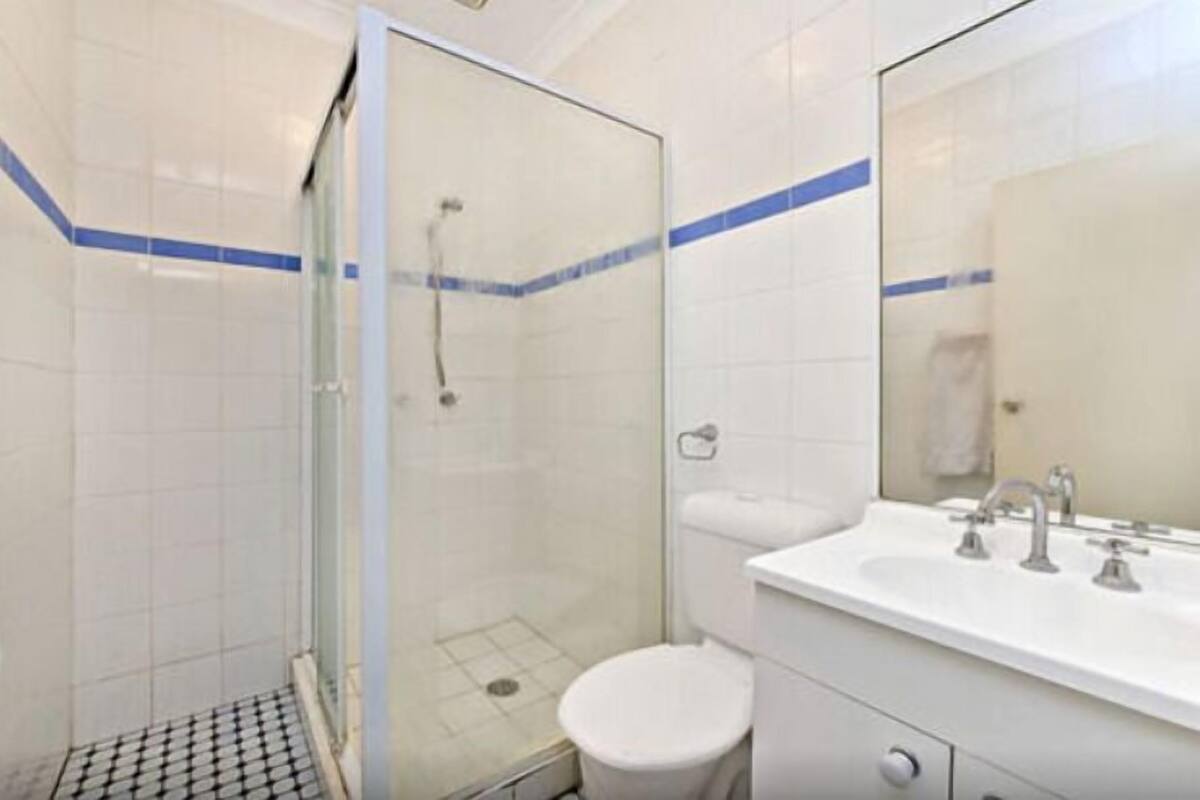 A bathroom with a glass-enclosed shower, a white sink with a mirror, and a toilet.