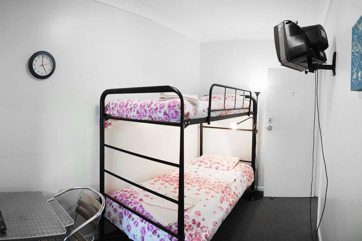 A dormitory room with bunk beds, a desk, a chair, a window with bars, a clock, and a lamp.