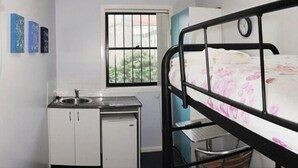 A compact room with a bed, a small desk, a sink, and a window. - Sinclairs City Hostel (Surry Hills)
