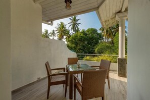 A balcony with a glass table and wicker chairs, overlooking a garden with palm trees. - Deltora Boutique Hotel (Galle)