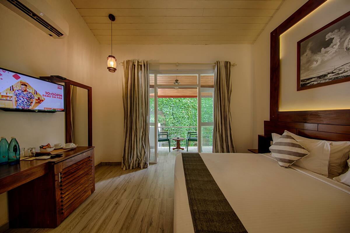 Ein Hotelzimmer mit Bett, Fernseher, einem Holzkleiderschrank, einem Schreibtisch und einem Balkon mit Tisch und Stühlen.