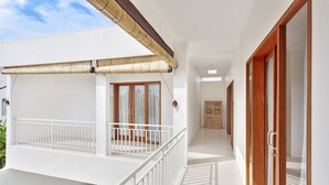 A hotel corridor with a balcony, wooden doors, and a ceiling fan. - Villa Kirana (Seminyak)