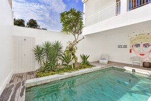 Una piscina con borde de azulejos, rodeada de plantas y un mural.