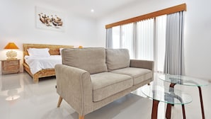 A modern bedroom with a beige sofa, a glass coffee table, a wooden bed, and a painting of ducks on the wall. - Villa Kirana (Seminyak)