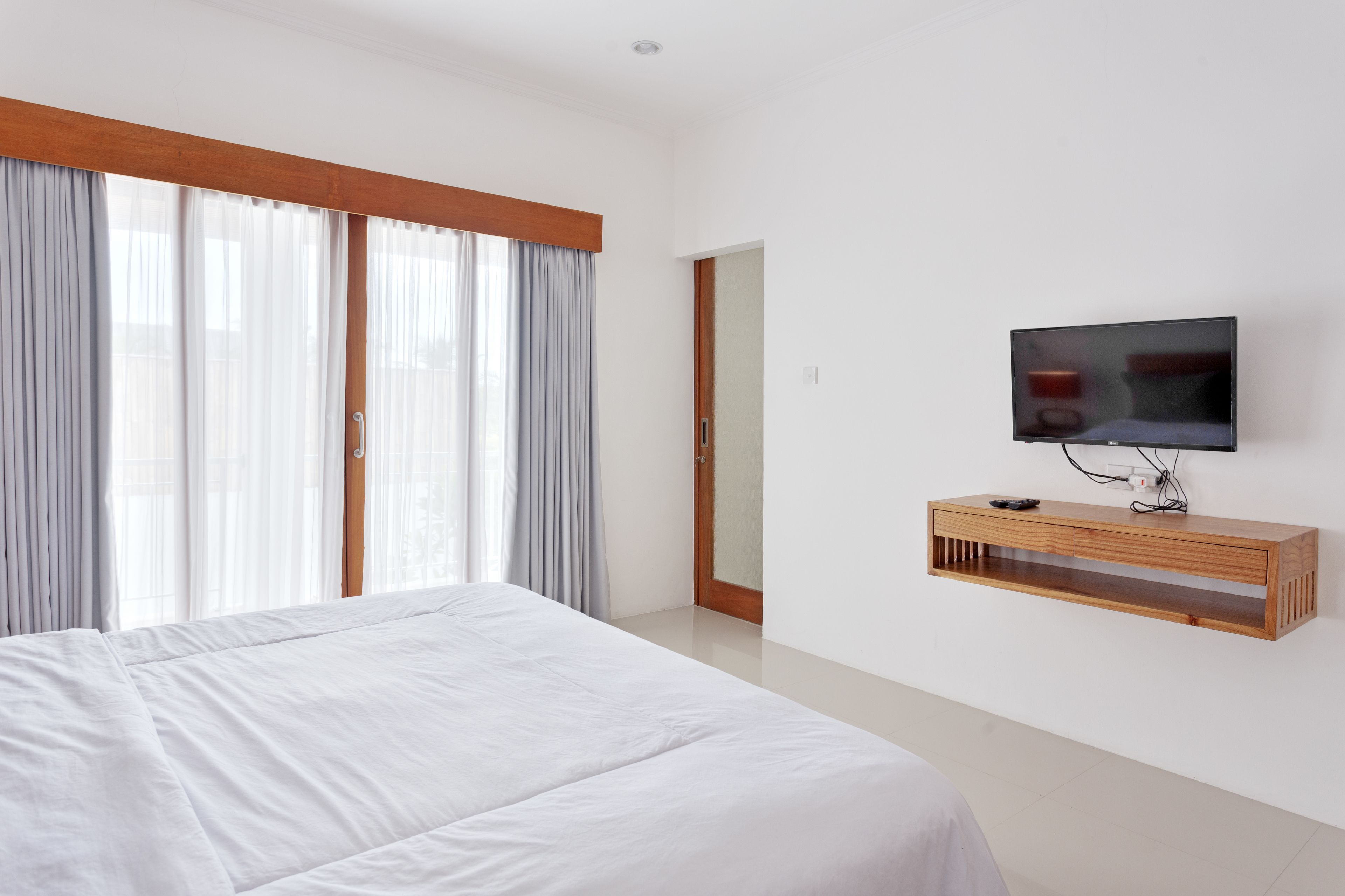 A modern hotel room with a large bed, a TV mounted on the wall, and a wooden console table.