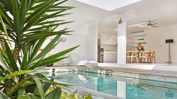 A modern indoor pool area with a clear view of the adjacent dining space, featuring a table and chairs. - Villa Kirana (Seminyak)