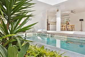 Zona de piscina interior moderna amb una vista clara de la zona de menjador propera, que inclou una taula i cadires.