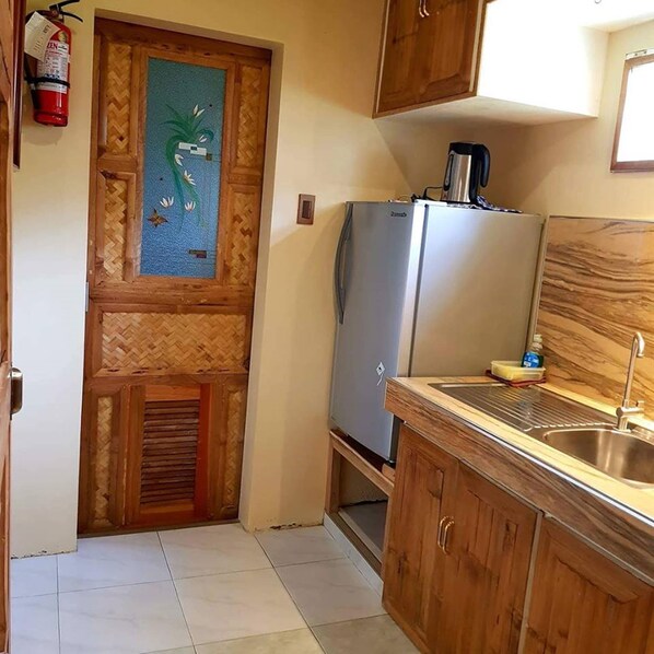 Cocina compacta con refrigerador, lavamanos y un mueble de madera.
