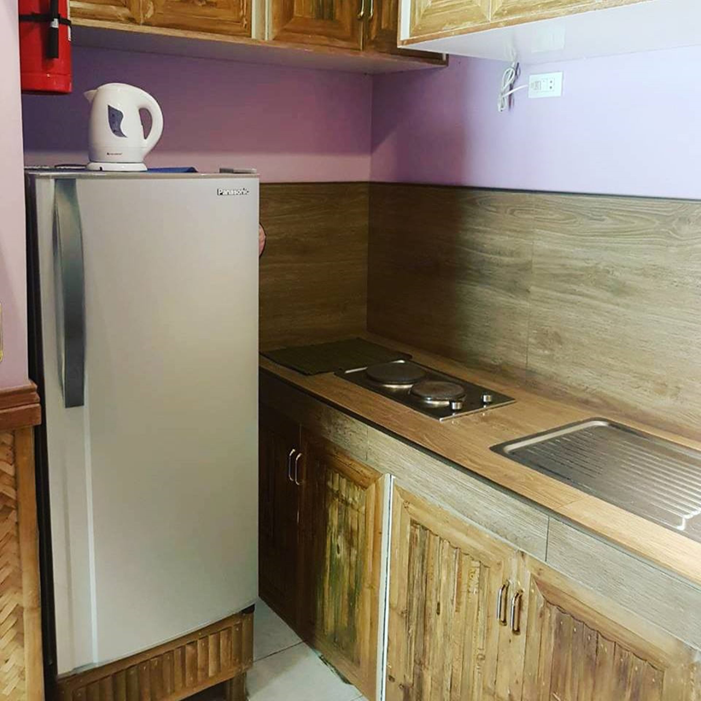 A compact kitchen with a refrigerator, a sink, and wooden cabinets.