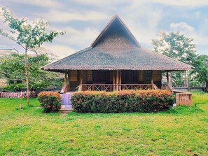 Una cabaña tradicional con techo de paja, un porche de madera y un jardín bien cuidado al frente.