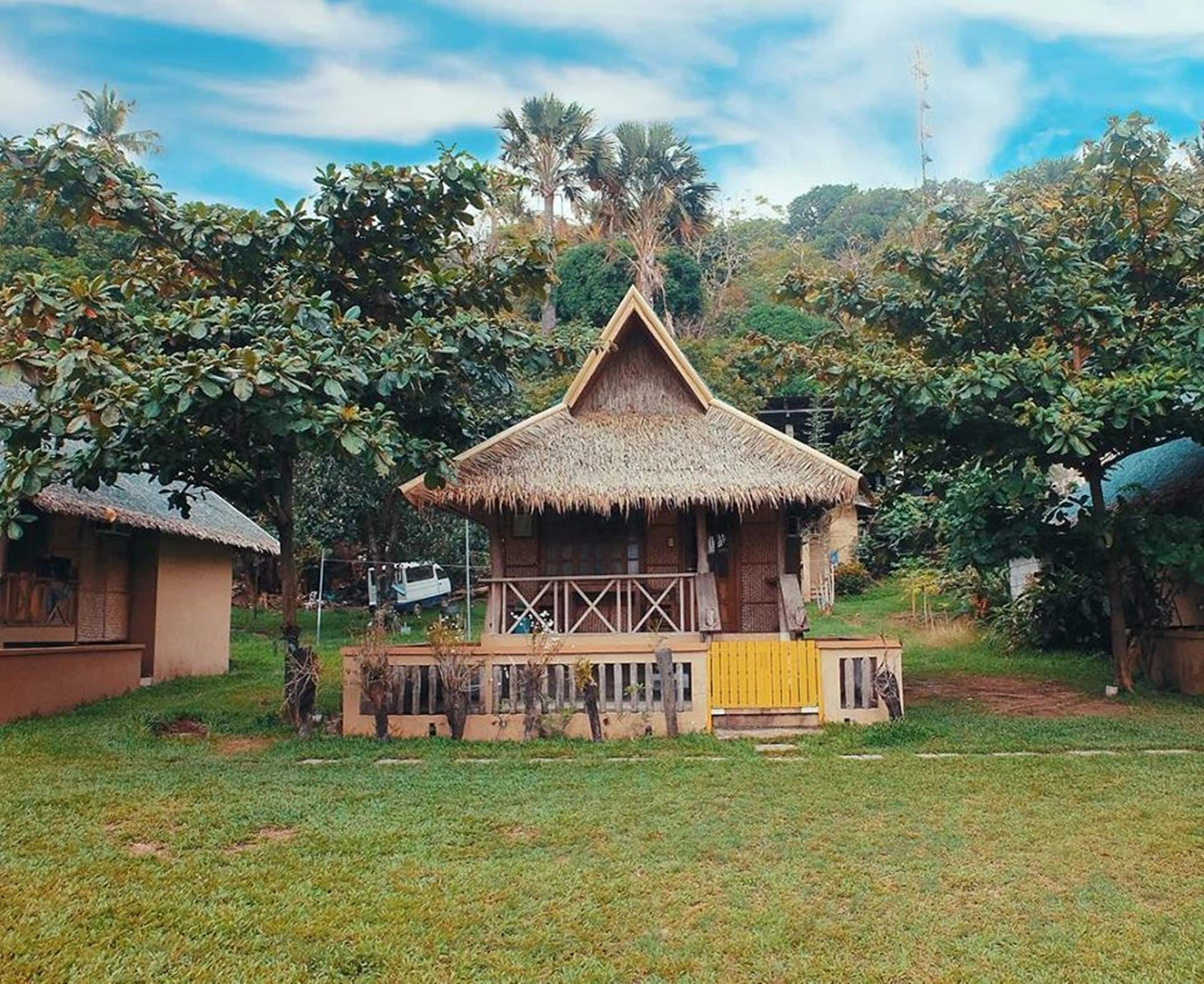 A thatched-roof hut with a wooden porch, surrounded by lush greenery.
