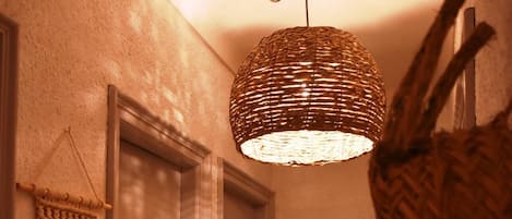 Um corredor com luminária trançada, um pendente de macramé e um espelho refletindo o ambiente.
