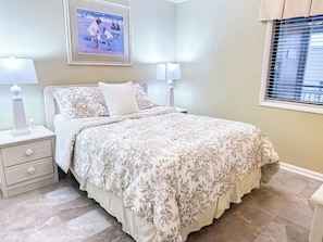 A bedroom with a bed, nightstands, lamps, a framed picture on the wall, and a window with blinds.