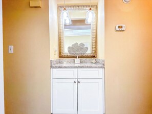A bathroom with a white vanity, a mirror with a decorative frame, and two pendant lights.