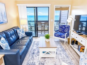 Ein Wohnzimmer mit Sofa, Sessel, Couchtisch, Fernseher und einem Balkon mit Aussicht.