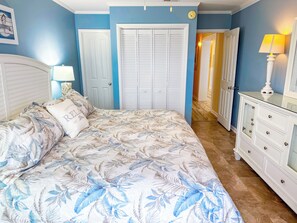 Une chambre à coucher comprenant un lit, une table de chevet, une commode et une porte donnant sur une autre pièce.
