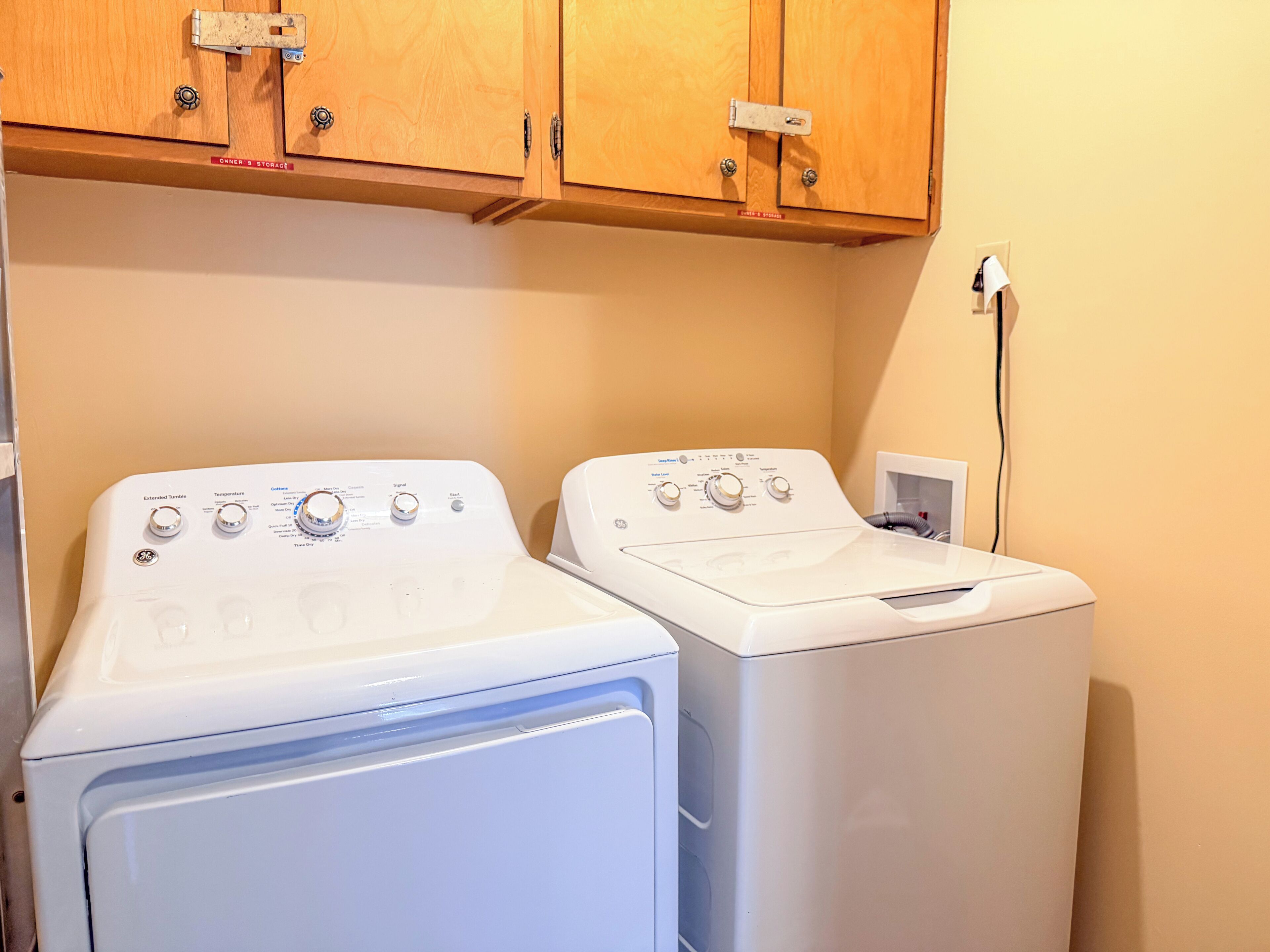 Two front-loading washing machines in a laundry room with wooden cabinets above.