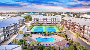 A hotel with a tennis court, pool, and multiple balconies.