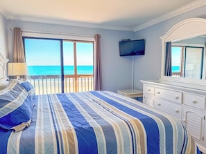 A hotel room with a large bed, a television, a dresser, and a view of the ocean.