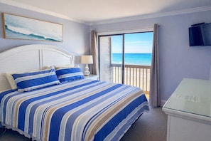 Een hotelkamer met een bed, een televisie, een schilderij en een balkon met uitzicht op zee.