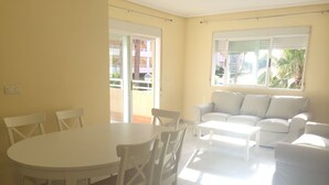 A bright living room with a white table and chairs, a sofa, and large windows with a view of a building and greenery. - 3 bedrooms and 2 full bathrooms, very comfortable and well equipped. (Denia)