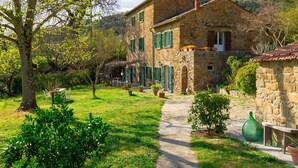 Une maison en pierre avec un chemin de jardin menant à l’entrée, entourée de verdure et sous un ciel dégagé.