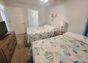 Un dormitorio con dos camas, un aparador, una lámpara y una puerta que da a otra habitación.