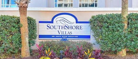 A sign for SouthShore Villas with a clear view of the building's facade and a landscaped area with various plants.