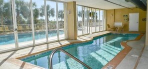 Una piscina interior con paredes de vidrio transparente, suelo de baldosas y escalera de acceso.
