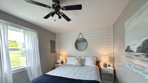 A bedroom with a bed, two bedside tables with lamps, a ceiling fan, a window with curtains, and a wall-mounted mirror. - River Front Property With Water View, Minutes To Brackley, & Screened In Dining (Oyster Bed)