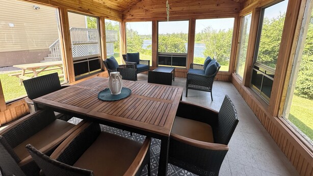 A covered outdoor area with a wooden ceiling, large windows, and a table with chairs. - River Front Property With Water View, Minutes To Brackley, & Screened In Dining (Oyster Bed)