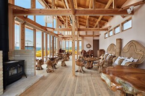 Una habitación amplia con techo alto, vigas de madera, ventanas grandes y chimenea.
