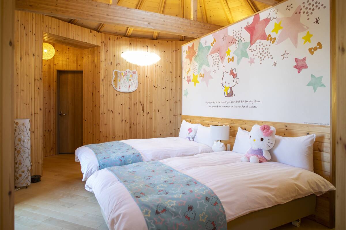Une pièce chaleureuse en bois, avec deux lits, un mur décoré de motifs en forme d’étoiles et des décorations à l’effigie de Hello Kitty.