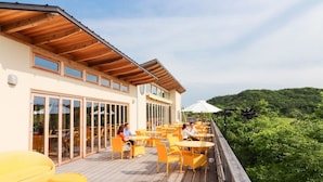 Terraza exterior con sillas y mesas amarillas, con vistas a una ladera boscosa.