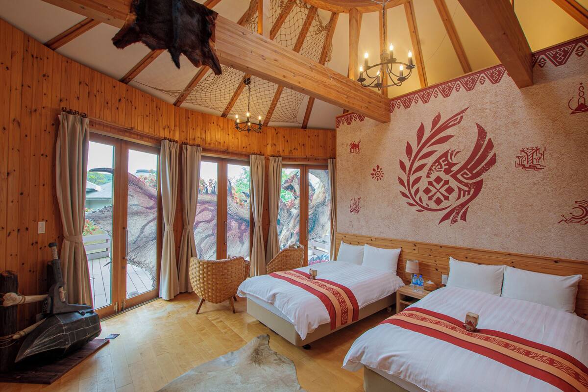 Une cabane en bois avec deux lits, une cheminée et de grandes fenêtres.