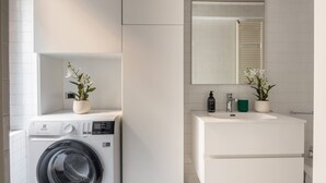 Ein modernes Badezimmer mit Waschmaschine, Waschbecken und zwei Zimmerpflanzen.
