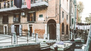A canal with boats docked, a brick building with a sign reading "CAMPAZZO DE L'ERBA," and laundry hanging on a line. - Zattere Design Loft R&R (Venecia)