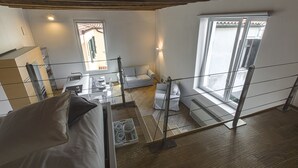 A high-ceilinged room with a wooden floor, a sofa, a dining table, and a window with a view. - Zattere Design Loft R&R (Venecia)